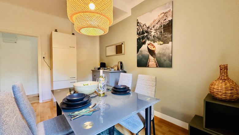 Esszimmer mit Glastisch, grauen St&uuml;hlen und gro&szlig;em Lampenschirm.