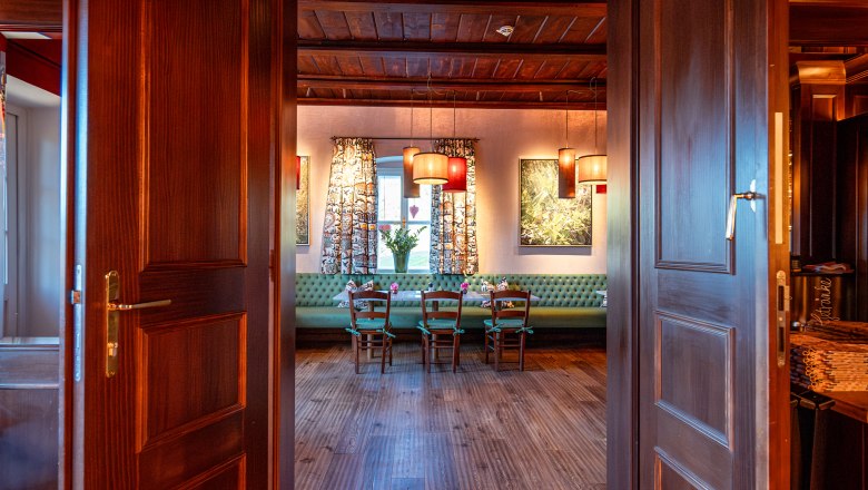 Blick durch ge&ouml;ffnete Holzt&uuml;ren in einen gem&uuml;tlichen Raum mit Holzboden, Tisch und St&uuml;hlen, dekoriert mit Lampen und Vorh&auml;ngen.