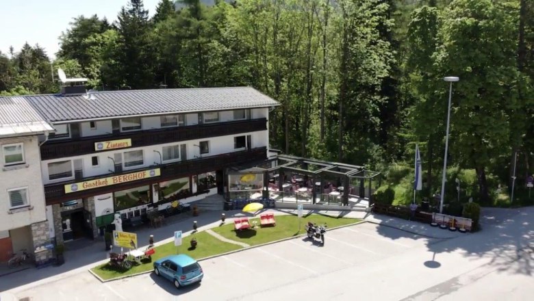 Außenansicht des Gasthofs Berghof mit Terrasse und Parkplatz, umgeben von Bäumen.