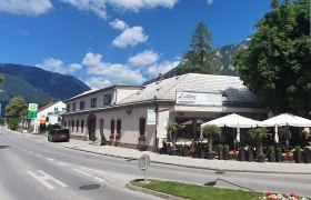Straßenszene mit Restaurant L'attore und Bergen im Hintergrund.