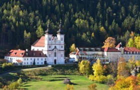 Die Wallfahrtskirche Maria Schutz vor einem bewaldeten Hügel im Herbst.