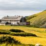 Das Karl-Ludwig-Haus in einer alpinen Landschaft mit gelben Blumenwiesen und bewölktem Himmel.