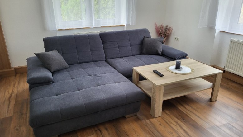 Wohnzimmer mit grauem Ecksofa und Holztisch vor einem Fenster.