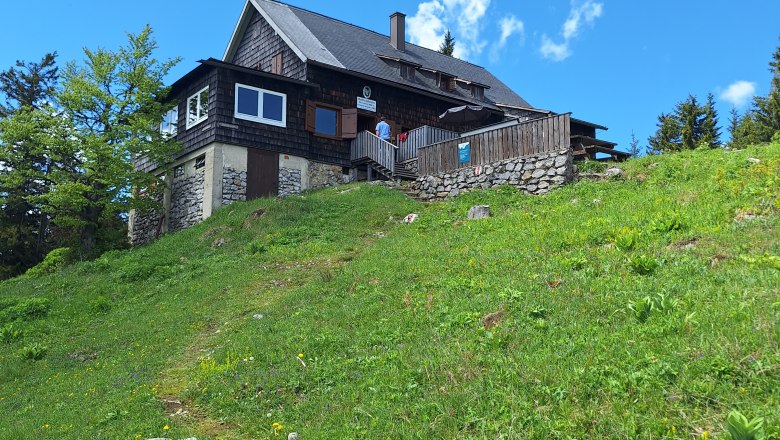urige Hütte am Berg, davor grüne saftige Wiese