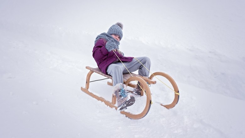 Kind in Winterkleidung sitzt auf einem Holzschlitten im Schnee.