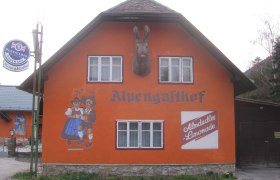 Orange gestrichenes Geb&auml;ude mit der Aufschrift 'Alpengasthof', Wandmalerei von tanzendem Paar und Almdudler-Werbung.