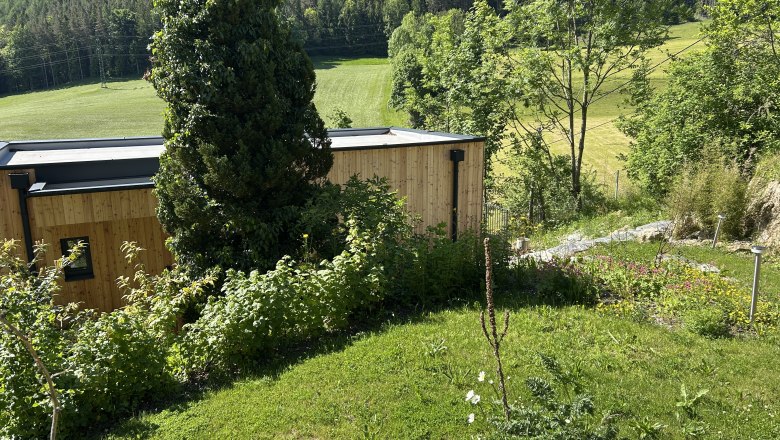 Holzhaus in grüner Landschaft mit Bäumen und Wiese.