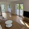 Modernes Wohnzimmer mit Holzboden, Sofa, Sessel, Couchtisch und Fernseher.