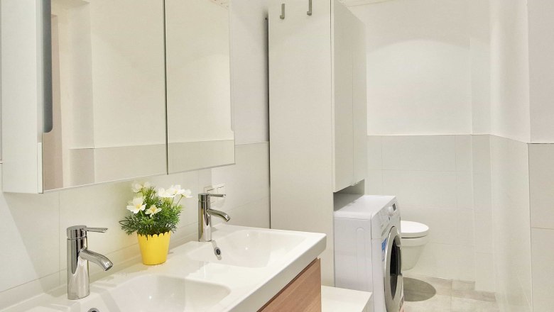 Modernes Badezimmer mit Doppelwaschbecken, Spiegel, Waschmaschine und WC.