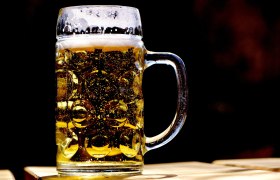 Ein voller Bierkrug mit goldenem Bier und Schaumkrone, beleuchtet von Sonnenlicht, steht auf einem Tisch.