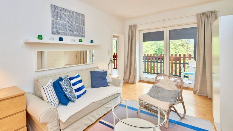 Modernes Wohnzimmer mit Sofa, Kissen, Glastisch und Balkon.