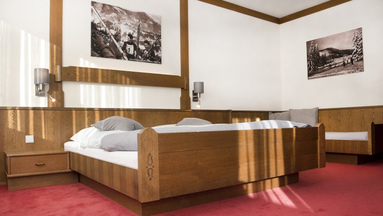 Ein Schlafzimmer mit einem h&ouml;lzernen Doppelbett, rotem Teppichboden und zwei schwarz-wei&szlig;en Bildern an der Wand.