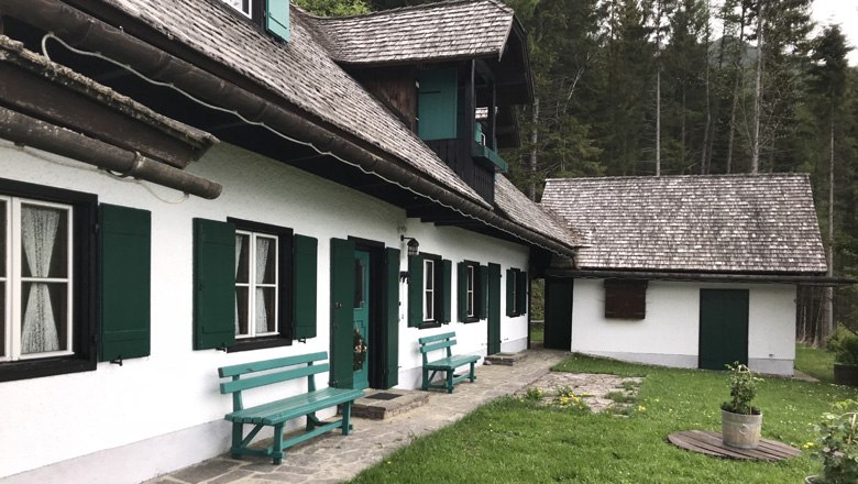 Ferienhaus Berghof Zifko, © Berghof Zifko Ein traditionelles Ferienhaus mit grünen Fensterläden und Holzbänken vor einem Wald.