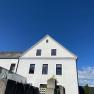Weißes Gebäude mit Giebeldach vor blauem Himmel.