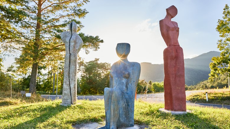 Drei bunte Skulpturen auf einer Wiese bei Sonnenuntergang.