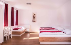 Helles Zimmer mit zwei Betten, roten Vorhängen und einem Bild an der Wand.