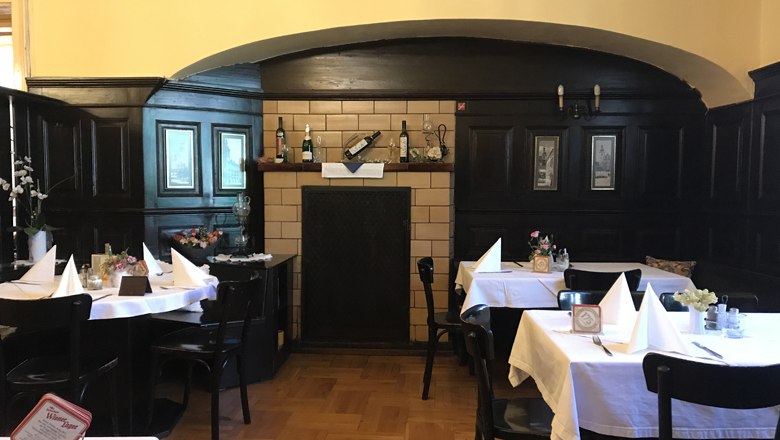 Innenansicht eines traditionellen Restaurants mit dunkler Holzvert&auml;felung und gedeckten Tischen.