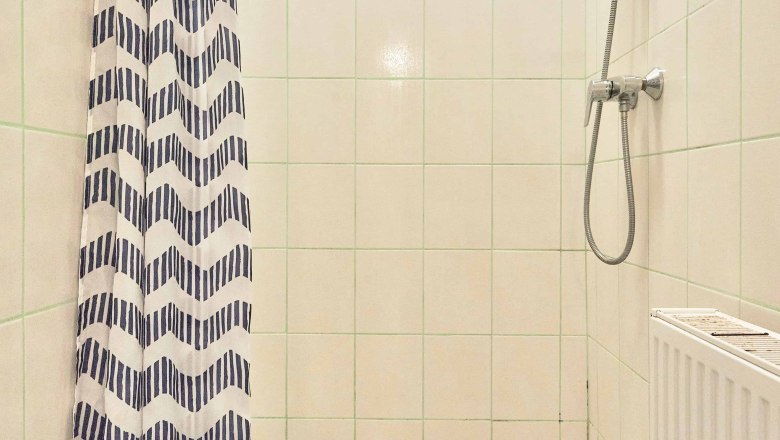 Dusche mit Duschvorhang und Handbrause in einem gefliesten Badezimmer.