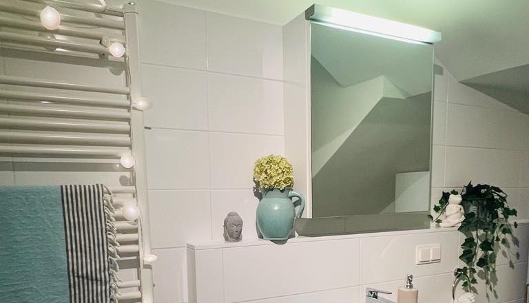 Modernes Badezimmer mit Waschbecken, Spiegel, Handtuchhalter und Dekorationen.