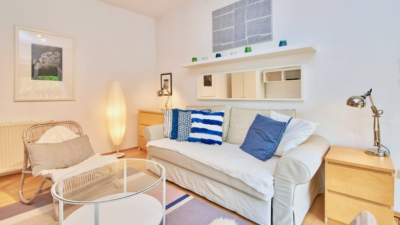 Gemütliches Wohnzimmer mit Sofa, Kissen, Sessel, Stehlampe und Couchtisch.