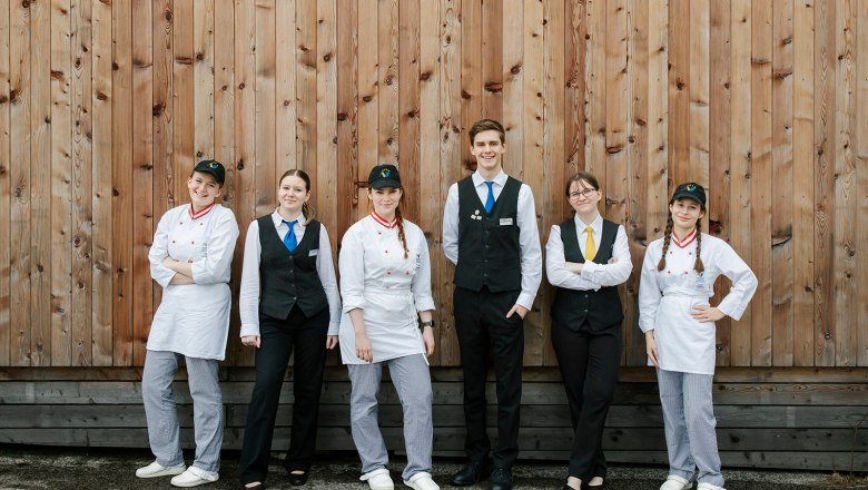 Sechs junge Menschen in Uniformen vor einer Holzwand.
