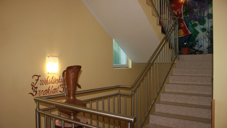 Treppenhaus mit Gel&auml;nder, Wanddekoration und Vase.