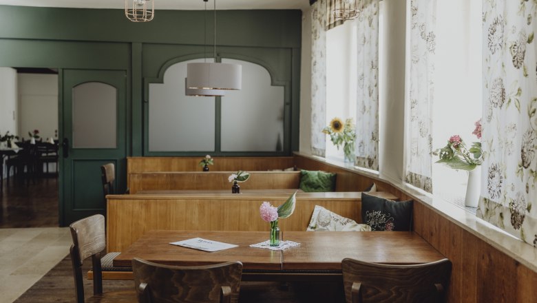 Innenansicht eines traditionellen Wirtshauses mit Holzmöbeln und Blumen auf den Tischen.