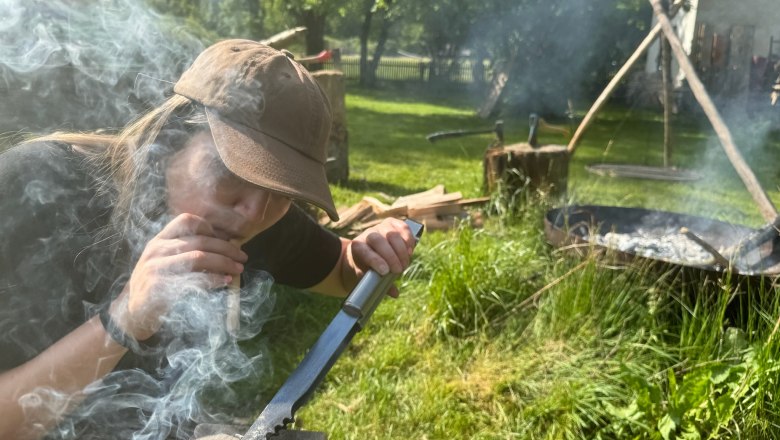 Person entzündet Feuer mit Messer und Holz im Freien.