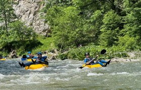 Personen beim Tubing auf einem Fluss in einer grünen, bewaldeten Umgebung.