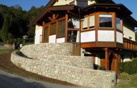 Haus mit Steinmauer und Holzverkleidung, umgeben von Bäumen.