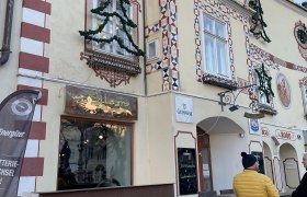Außenansicht des Cafe Allegro mit dekorierter Fassade und zwei Personen im Gespräch.