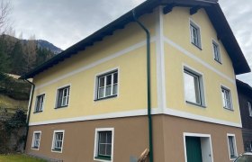 Zweist&ouml;ckiges gelb-braunes Haus mit wei&szlig;en Fensterrahmen und gr&uuml;nem Fallrohr.