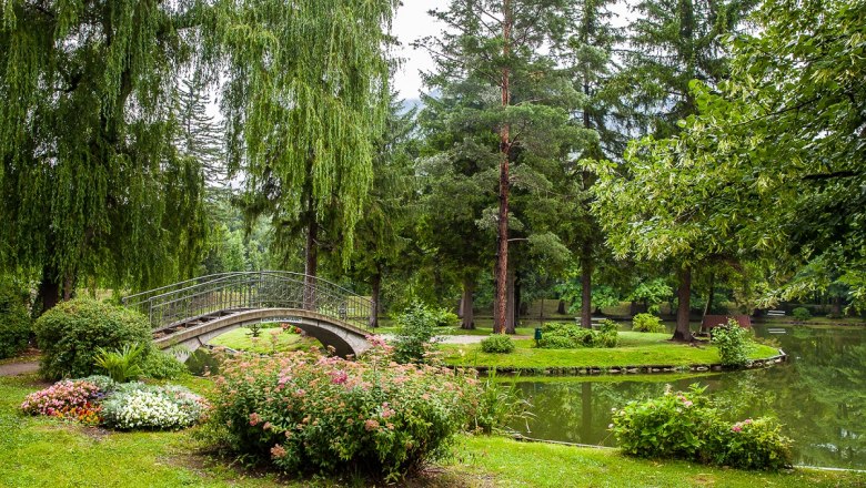 Ein idyllischer Park mit einer kleinen Brücke über einen Teich, umgeben von Bäumen und Blumen
