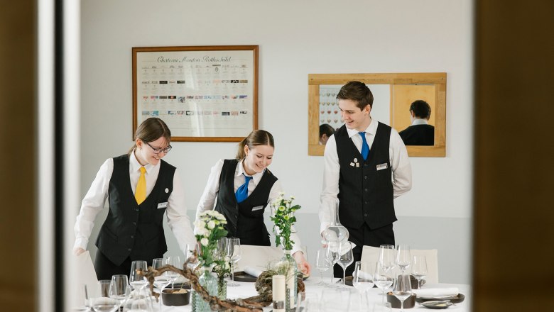 Drei Personen in Uniform decken einen Tisch in einem Schulungsraum ein.