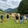 Gruppe von Menschen beim Axtwerfen im Freien vor Zielscheiben in einer bergigen Landschaft.