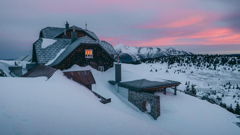 In der winterlichen Landschaft erstrahlt das Ottohaus in warmen Farben, w&auml;hrend die schneebedeckten Berge im Hintergrund majest&auml;tisch aufragen. Die ruhige Atmosph&auml;re l&auml;dt dazu ein, die frische Bergluft zu genie&szlig;en und die Sch&ouml;nheit der Wiener Alpen zu erleben.