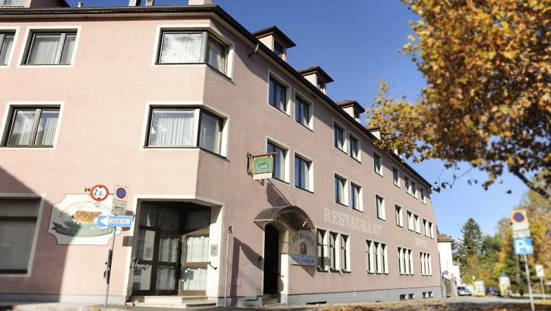 Außenansicht des Hotels Osterbauer mit rosa Fassade und Herbstlaub auf dem Boden.