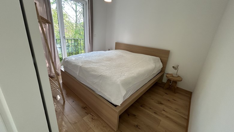Schlafzimmer mit Holzboden, Doppelbett und Fenster mit Blick ins Gr&uuml;ne.
