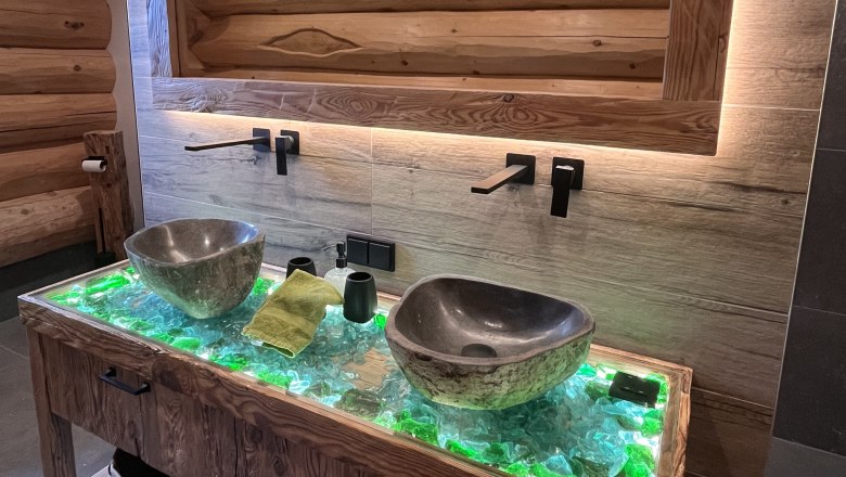Modernes Badezimmer mit zwei steinernen Waschbecken auf einem beleuchteten Holztisch.