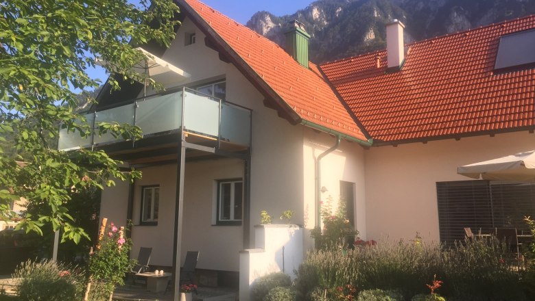 Ferienhaus mit Balkon und Garten vor Bergkulisse.
