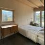 Schlafzimmer mit Bett, Holzdecke, Fenster mit Bergblick und Kommode.