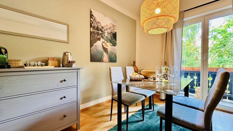 Gem&uuml;tliches Esszimmer mit Tisch, St&uuml;hlen und H&auml;ngelampe, Blick auf Balkon und Natur.