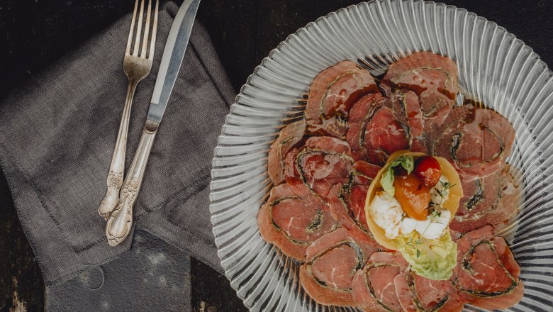 Ein Teller mit d&uuml;nn geschnittenem Fleisch und einer kleinen Salatgarnitur in der Mitte, daneben Besteck auf einer Serviette.