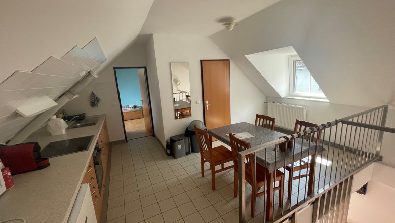 Wohnküche mit Esstisch, Stühlen, Küchenzeile und Dachschräge.