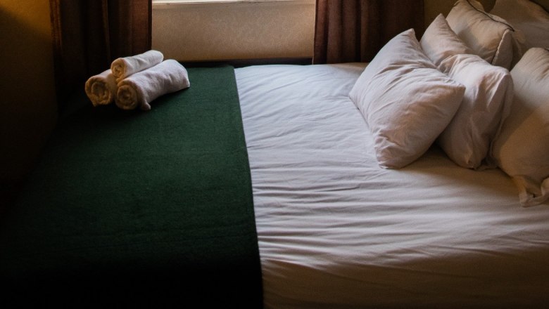 Ein gemütliches Schlafzimmer mit einem Bett, das vor einem Fenster steht. Draußen sind Bäume und ein Hausdach zu sehen.