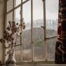 Blick aus einem Fenster mit Berglandschaft im Hintergrund, Vase mit Trockenblumen im Vordergrund.