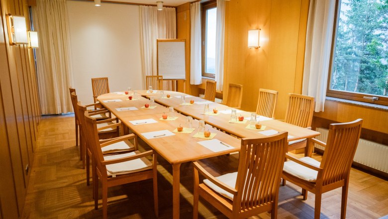 Ein Seminarraum mit einem langen Holztisch, umgeben von Stühlen. Auf dem Tisch liegen Notizblöcke, Stifte und Äpfel.