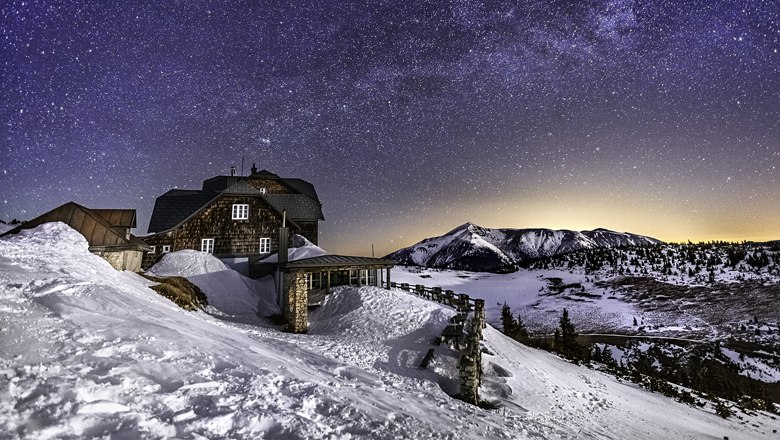 Berghütte im Schnee unter einem klaren Sternenhimmel.