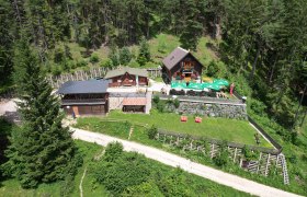 Luftaufnahme der Potschacherh&uuml;tte in einem Waldgebiet mit umliegenden B&auml;umen und einer Terrasse mit Sonnenschirmen.
