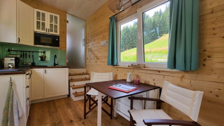 Kleine Küche mit Essplatz und Fenster mit Blick auf Wiese und Wald.